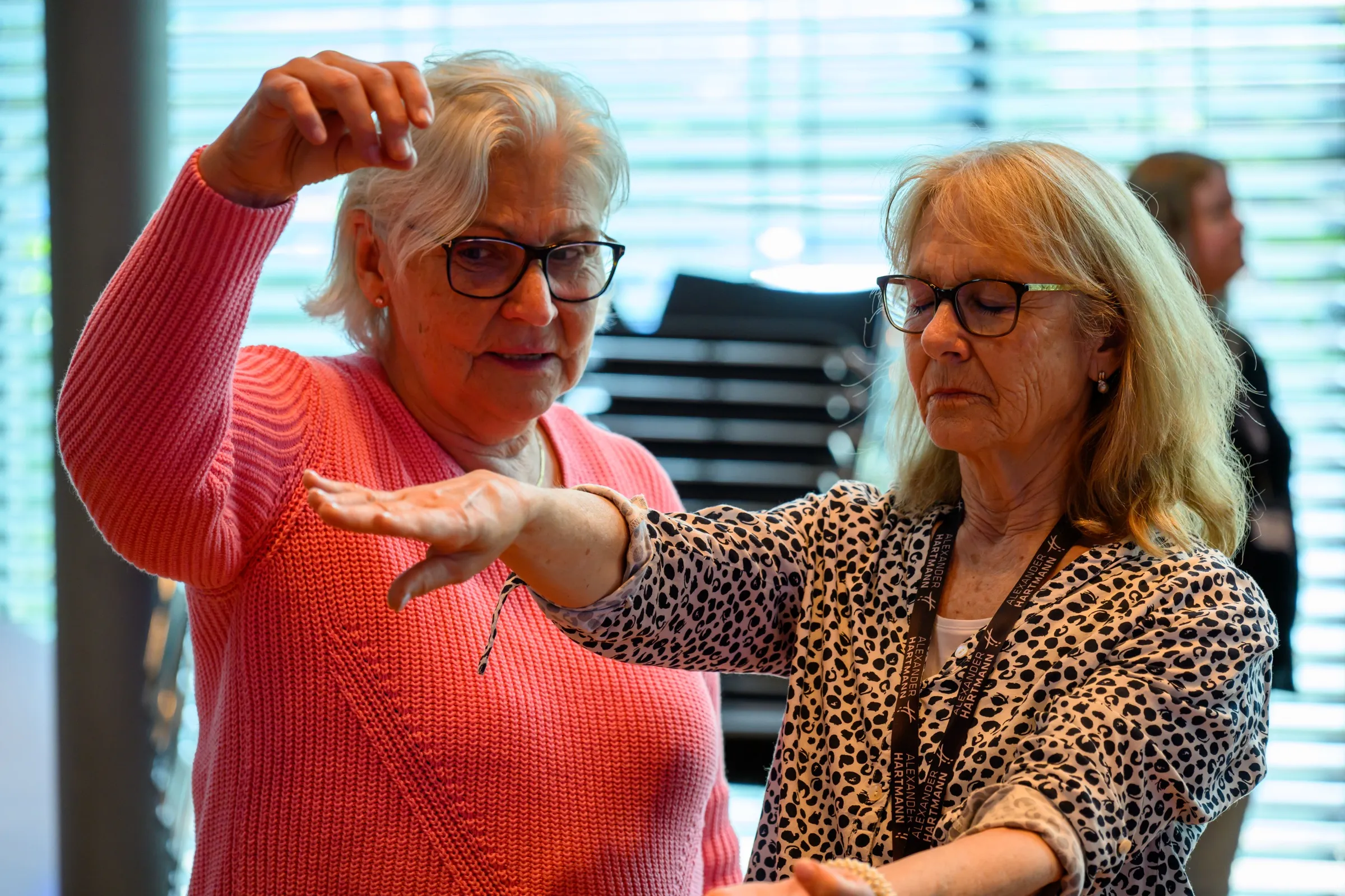 Zwei Teilnehmerinnen üben die Armlevitation: Eine hält ihre Hand über den schwebenden Arm der anderen, die mit gesenktem Blick dasitzt